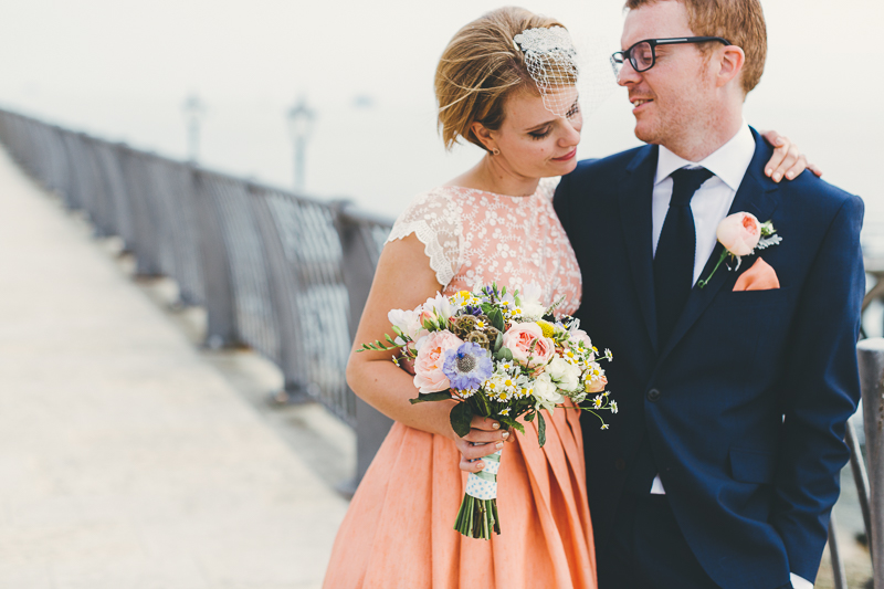 Natural wedding photos of Bride and groom in Old Portsmouth, bride wears peach, coral coloured wedding dress with cream beaded shoes and bouquet. Groom wears blue suit.