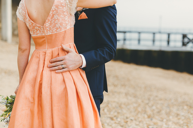 Natural wedding photos of Bride and groom in Old Portsmouth, bride wears peach, coral coloured wedding dress with cream beaded shoes and bouquet. Groom wears blue suit.