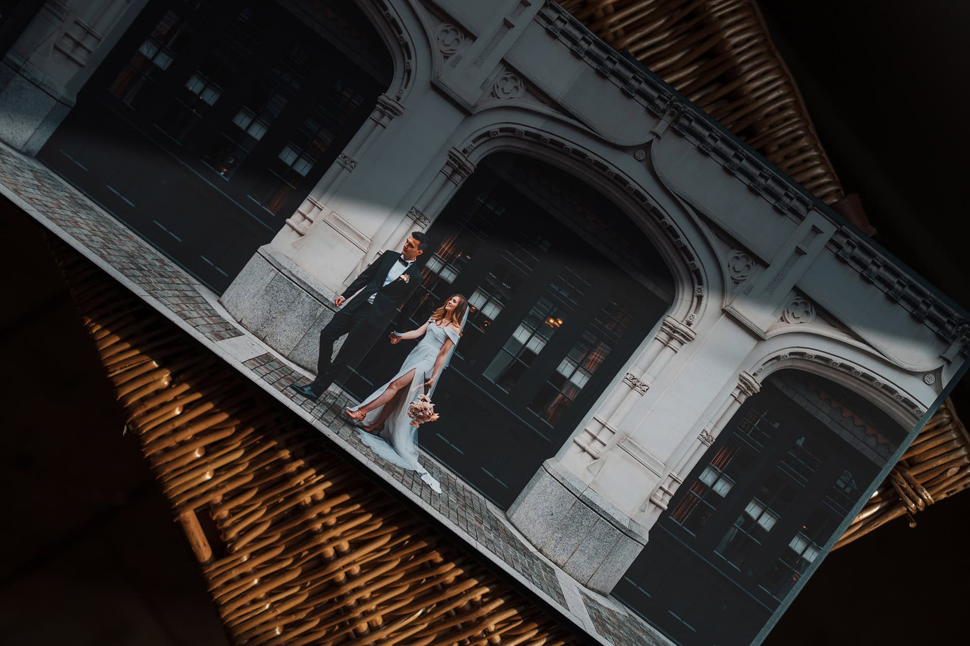 A spread from a beautiful fine art wedding album showing a couple walking through Marylebone outside the Chiltern Firehouse, bride wears modern slinky white dress with a big split. Book sits open on a wicker chest.